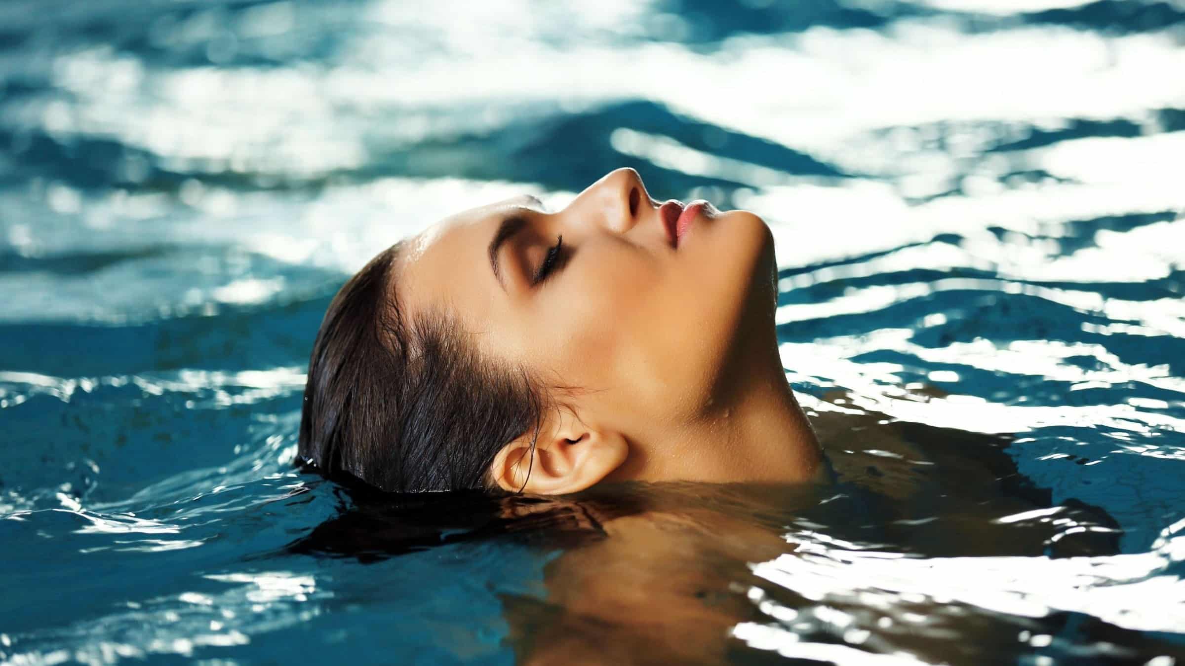 A woman floats with her head back and eyes closed in calm pool water